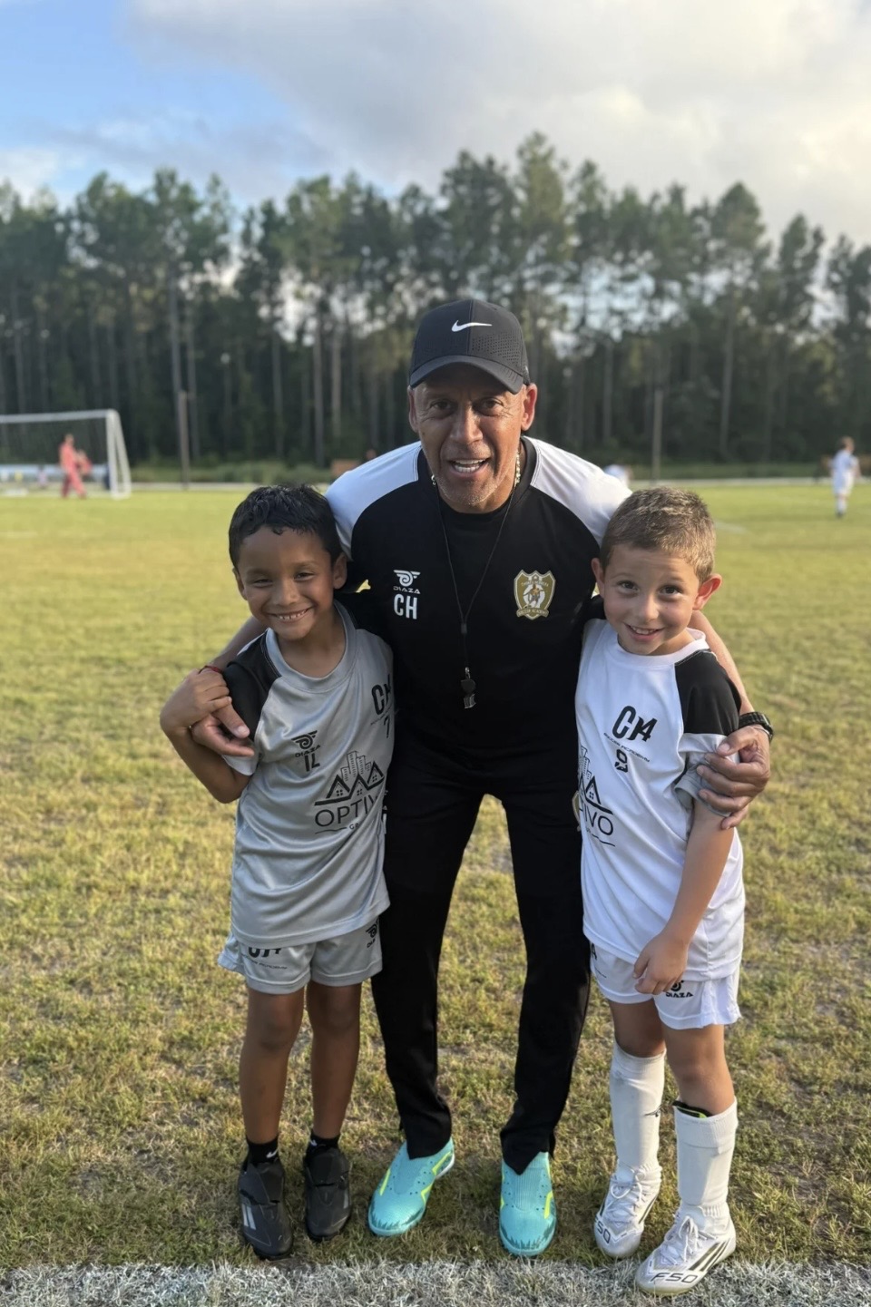 A CH4 coach poses with two smiling young players after training
